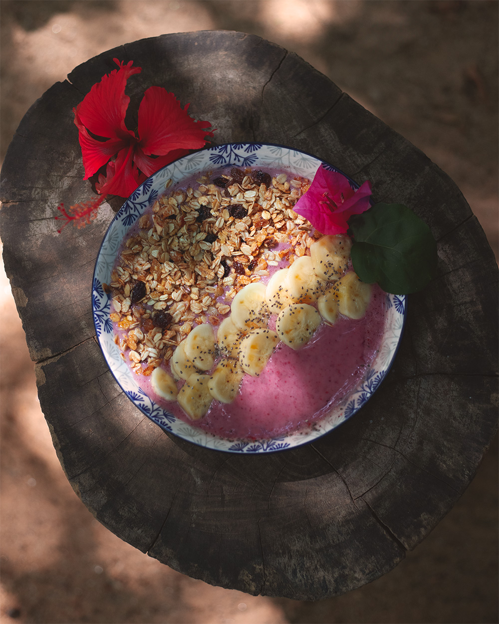 A smoothie bowl topped with banana, granola and flowers